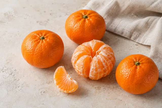 Clementine crude întregi, o clementină decojită și o felie
